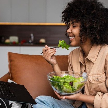 Stock Image of a woman sitting on a couch and eating a salad.