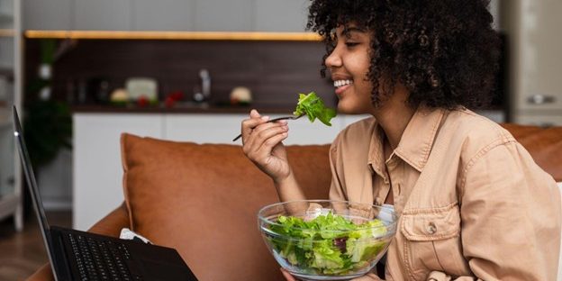 Stock Image of a woman sitting on a couch and eating a salad.