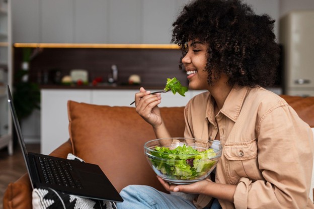 Stock Image of a woman sitting on a couch and eating a salad.